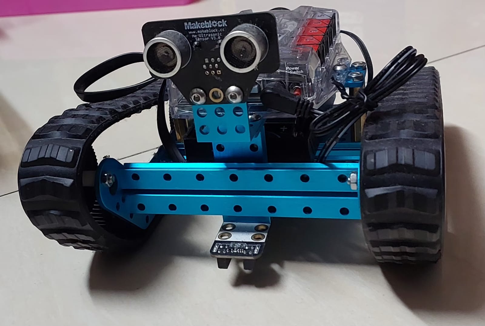 Front angle — dual ultrasonic sensor, line-follower module, and rugged rubber tracks.